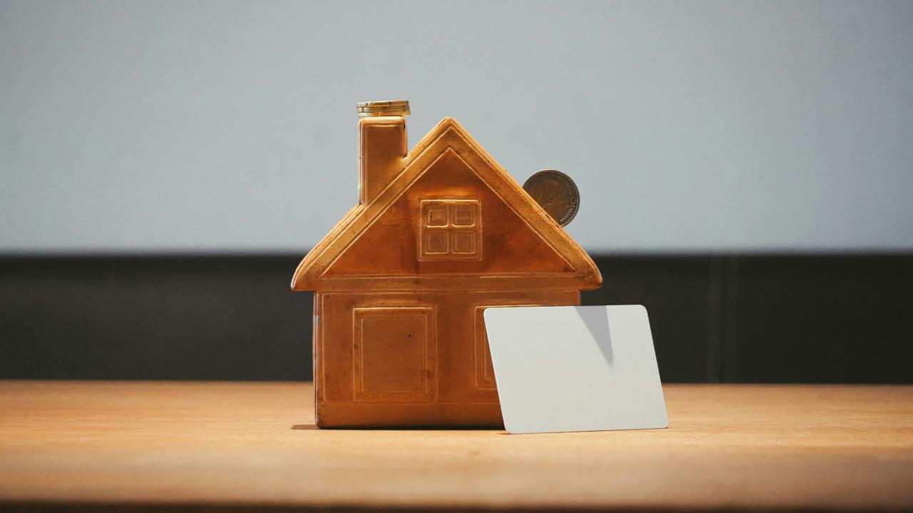 A small house bank with a coin and blank card.
